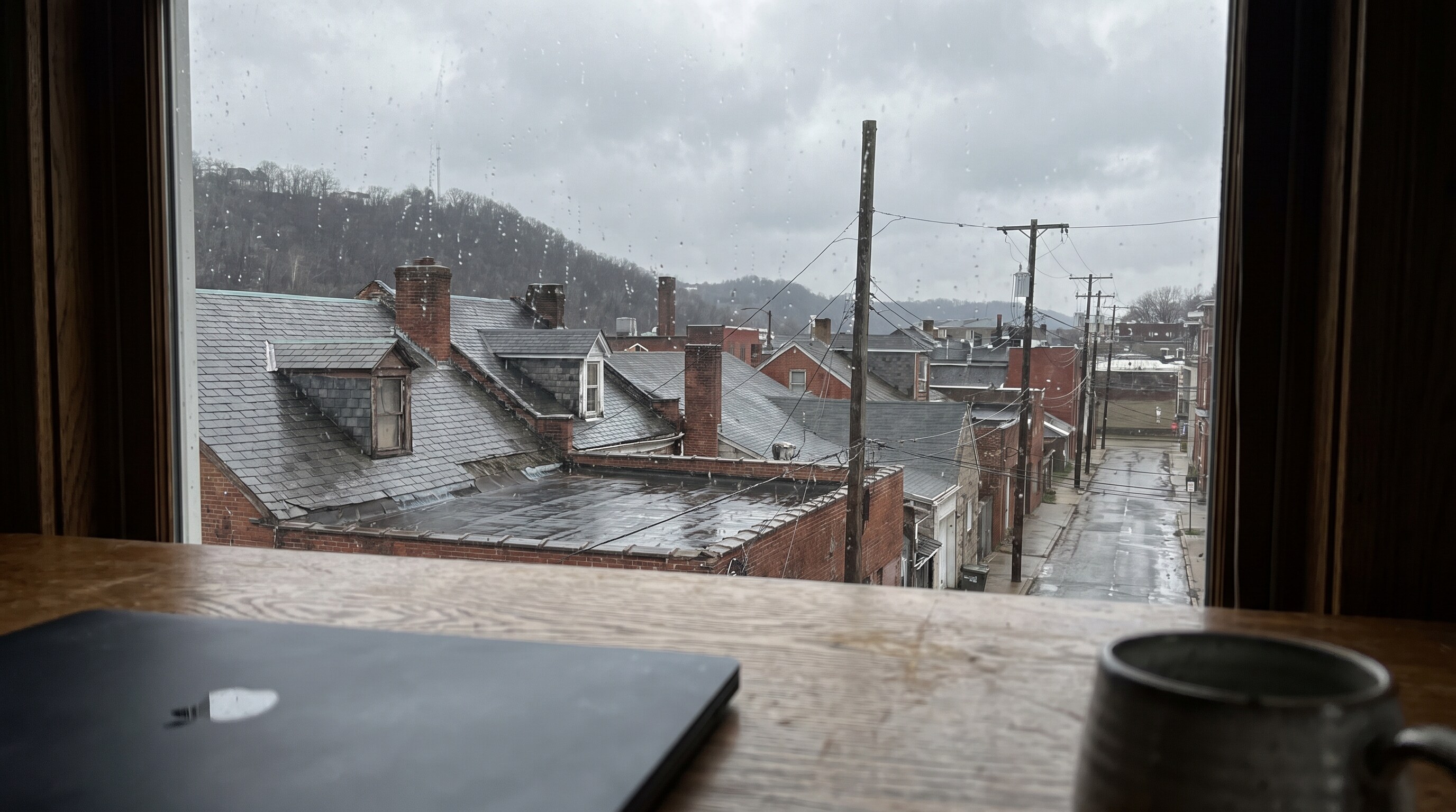 The view from a home office desk out over wet Pittsburgh rooftops under a low grey sky
